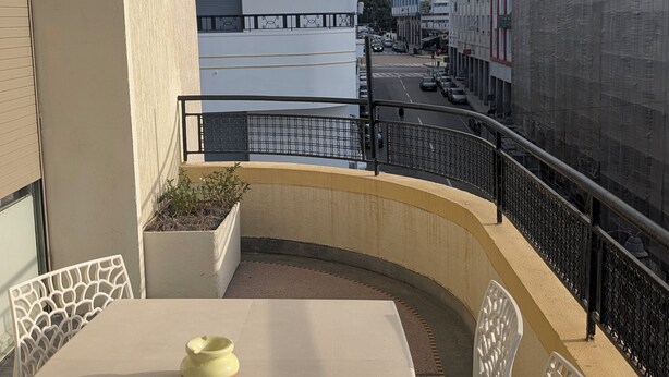 Un balcón con mesa y sillas, con vista a una calle con edificios y una mezquita.
