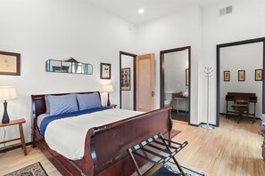 Ein Schlafzimmer mit einem hölzernen Bett, einem Nachttisch, einer Lampe, einem Spiegel und einem Klavier im angrenzenden Raum.