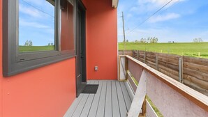 A balcony with a view of a green field, a red wall, and a wooden fence. - Riverside Retreat! Quiet and Charming 2 bed/2 bath (New Orleans)