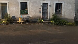 An old building with multiple windows, a small outdoor seating area with a round table and two chairs, and a door with a decorative panel.