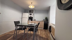 A compact kitchen with white appliances, a dining table with chairs, and a clock on the wall.