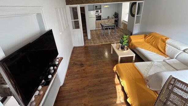 A living room with a TV, sofa, and coffee table. There is a kitchen in the background.