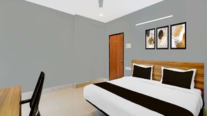 A hotel room with a bed, a desk, a chair, a ceiling fan, and artwork on the wall. - Deluxe Hotel Santosh Palace (Prayagraj)