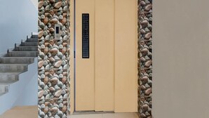 A beige door with a vertical window, surrounded by a stone wall, and a staircase to the left. - Deluxe Hotel Santosh Palace (Prayagraj)