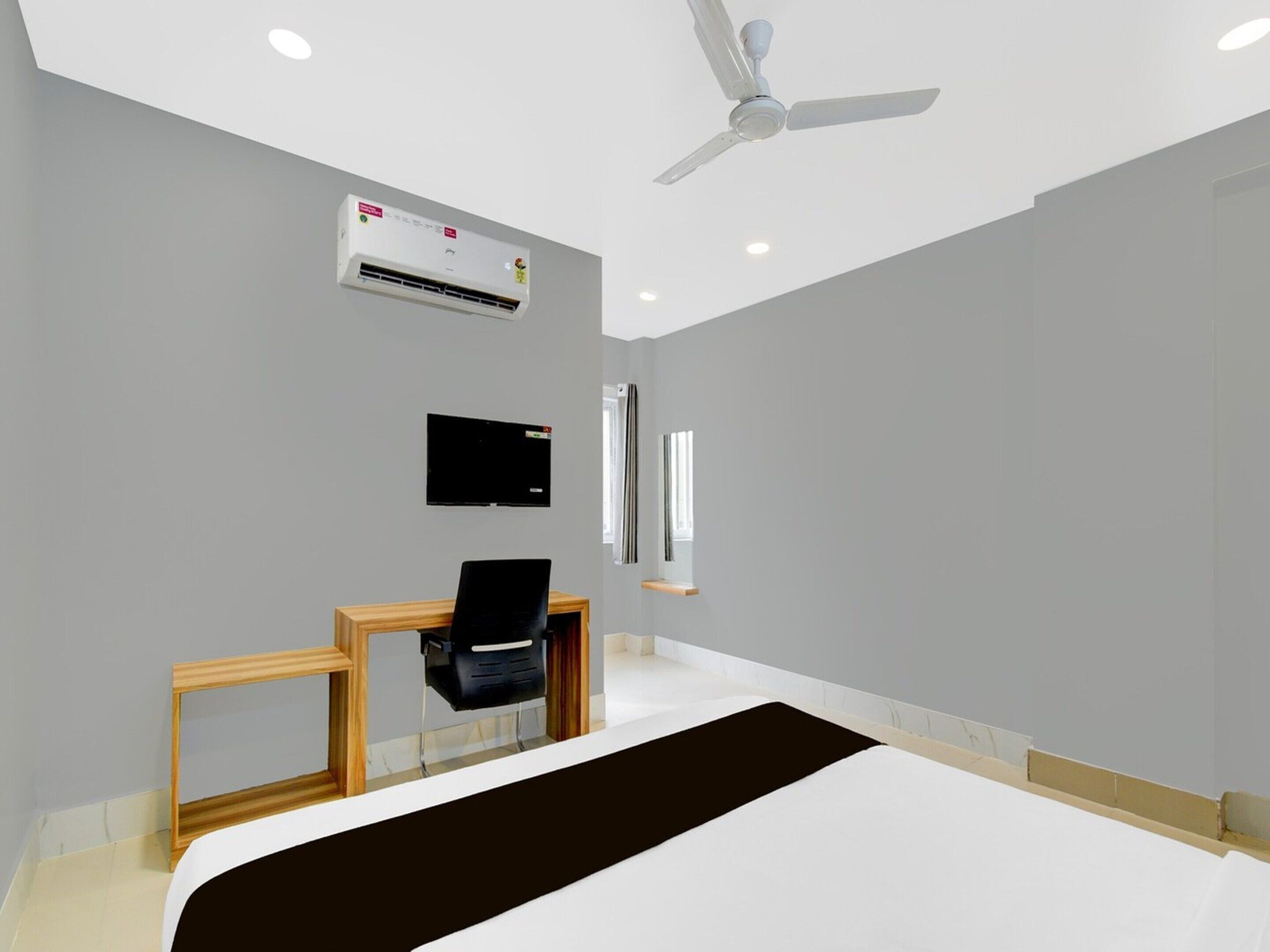 A hotel room with a bed, a desk with a chair, a television, an air conditioning unit, and a ceiling fan.