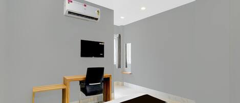 A hotel room with a bed, a desk with a chair, a television, an air conditioning unit, and a ceiling fan.