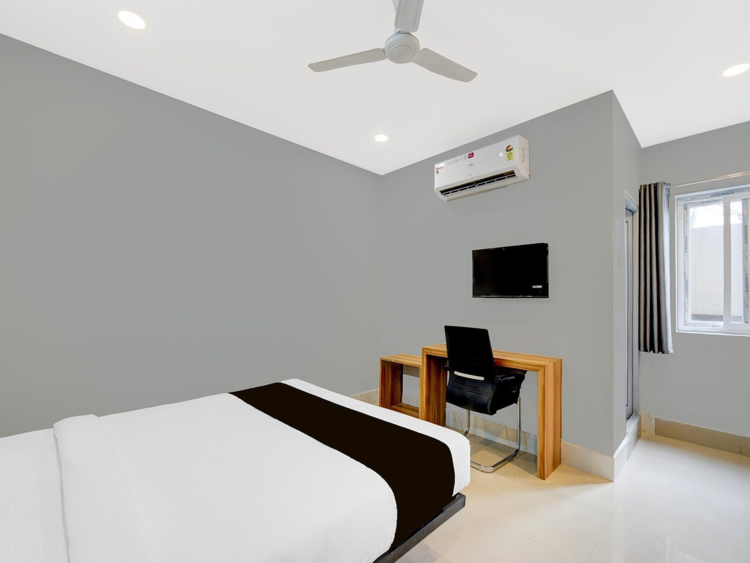 Une chambre d’hôtel moderne équipée d’un lit, d’un bureau, d’une chaise, d’une télévision, d’un climatiseur, d’un ventilateur de plafond et d’une fenêtre.