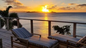 Sonnenuntergangblick von einem Balkon mit zwei Liegestühlen und einem Holzdeck.