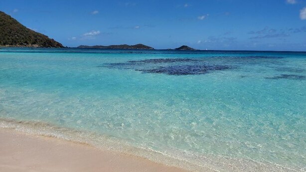 Ein Strand mit klarem türkisblauem Wasser, einem sandigen Ufer und fernen Inseln.