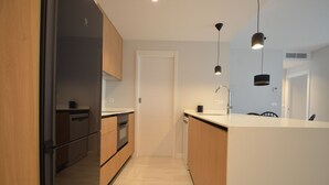Une cuisine moderne avec des meubles en bois, un réfrigérateur en acier inoxydable et des luminaires suspendus.