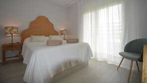 Une chambre à coucher avec un lit, deux lampes de chevet, une chaise et une fenêtre avec des rideaux légers.