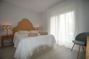 A bedroom with a bed, two bedside lamps, a chair, and a window with sheer curtains. - Los Colibries 2001 - Two Bedroom Apartment, Sleeps 5 (Punta del moral)