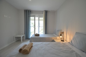Ein Hotelzimmer mit zwei Betten, einem kleinen Schreibtisch, einer Lampe und Blick durch eine Glastür.