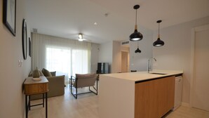 Ett modernt kök med en köksö i mitten, en matplats med soffa och stolar samt ett vardagsrum med TV och gardiner.
