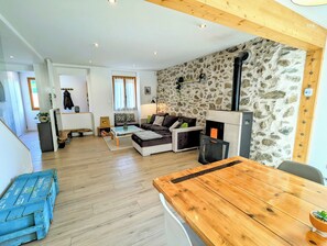 A cozy living room with a stone wall, a fireplace, a sofa, and a wooden dining table. - La Villa Fontaine: Heated Pool, Home Cinema & Sauna in the Heart of Belledonne (Saint-Martin-d'Uriage)