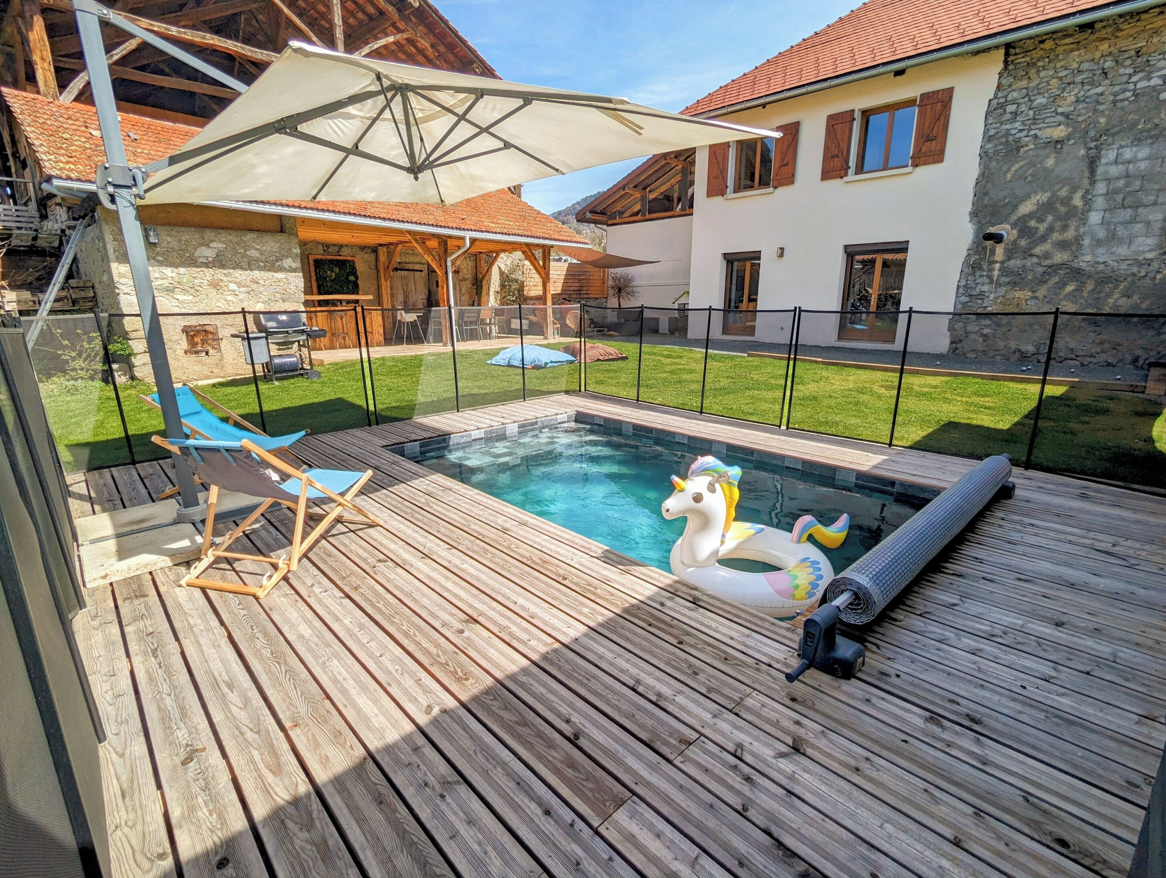 Une terrasse en bois avec une piscine, des licornes gonflables et un espace salon abrité.