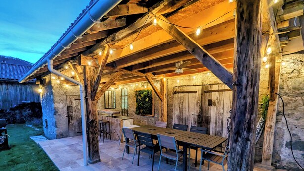 Patio esterno con tavolo e sedie di legno, pareti in pietra e luci decorative.