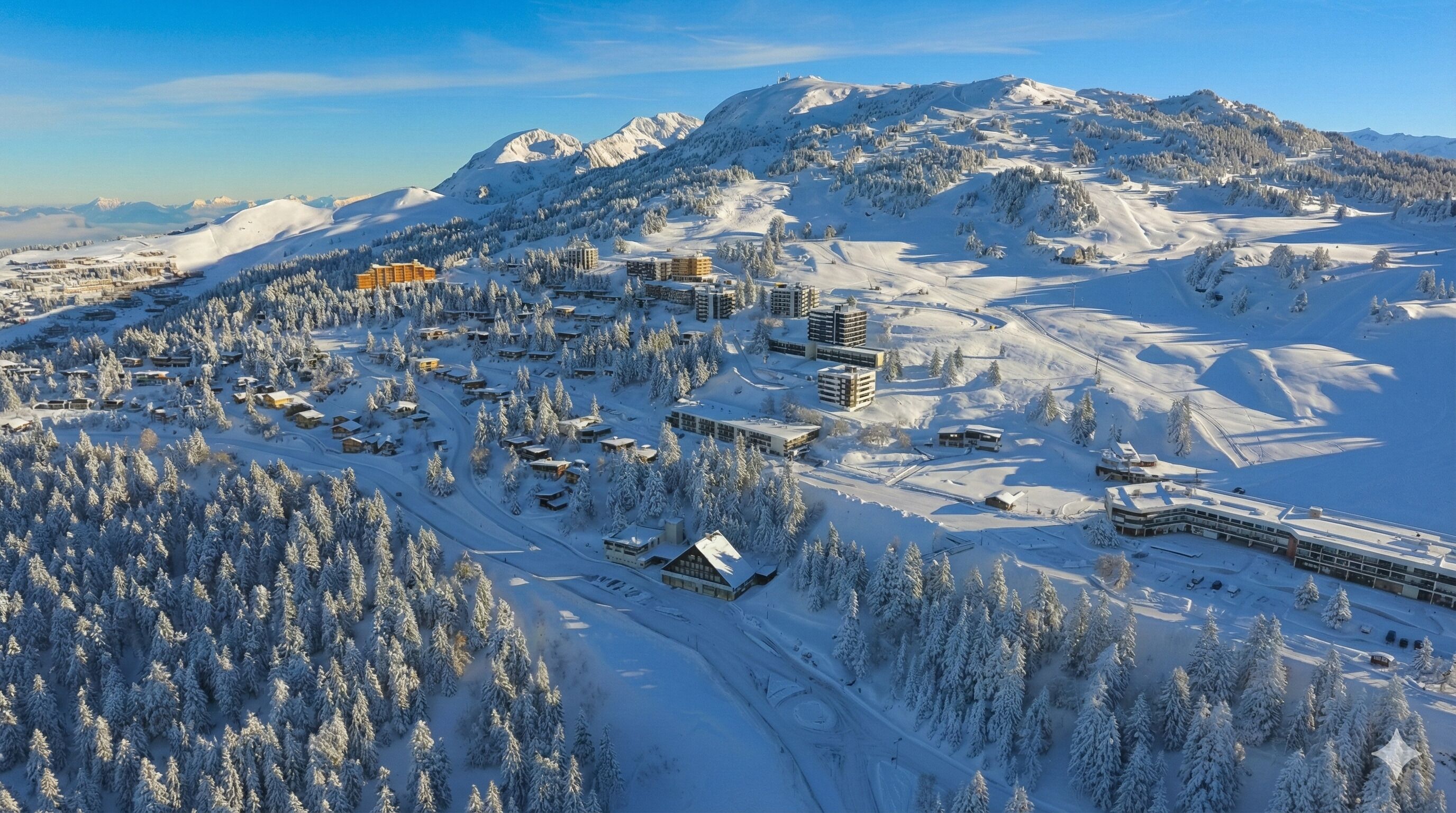 A snow-covered mountain resort with multiple buildings, ski slopes, and a dense forest.