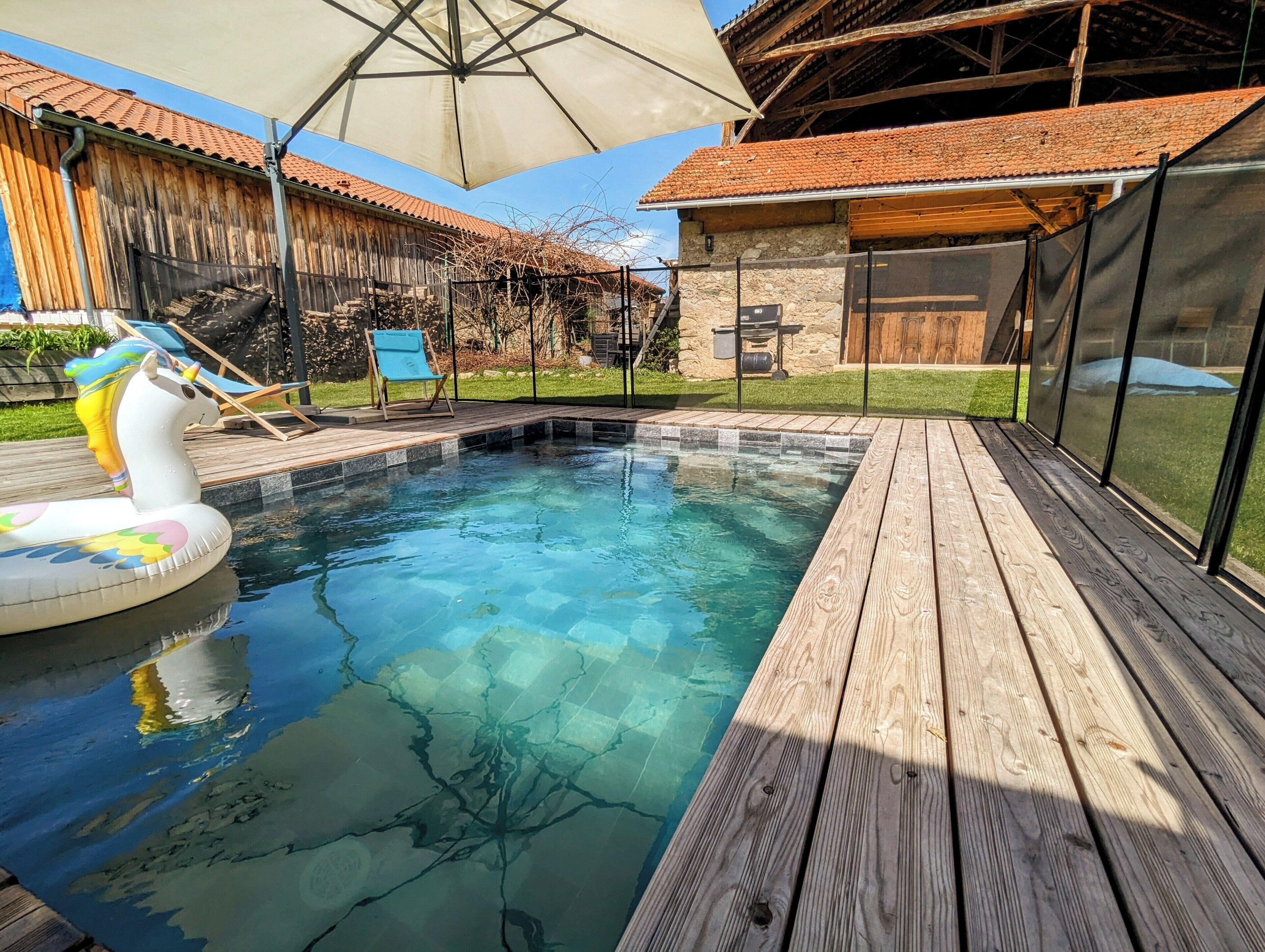 Une piscine dotée d’une terrasse en bois, de chaises longues et d’un espace abrité agrémenté d’une pergola.