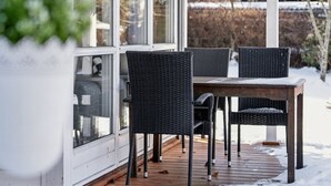Un espace extérieur abrité, doté d’une table et de chaises, d’une porte vitrée et offrant une vue sur un paysage enneigé.