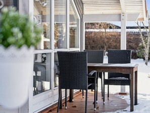 A covered outdoor seating area with a table and chairs, a glass door, and a view of a snowy landscape. - "Elenor" - 1.3km from the sea by Interhome (Græsted)