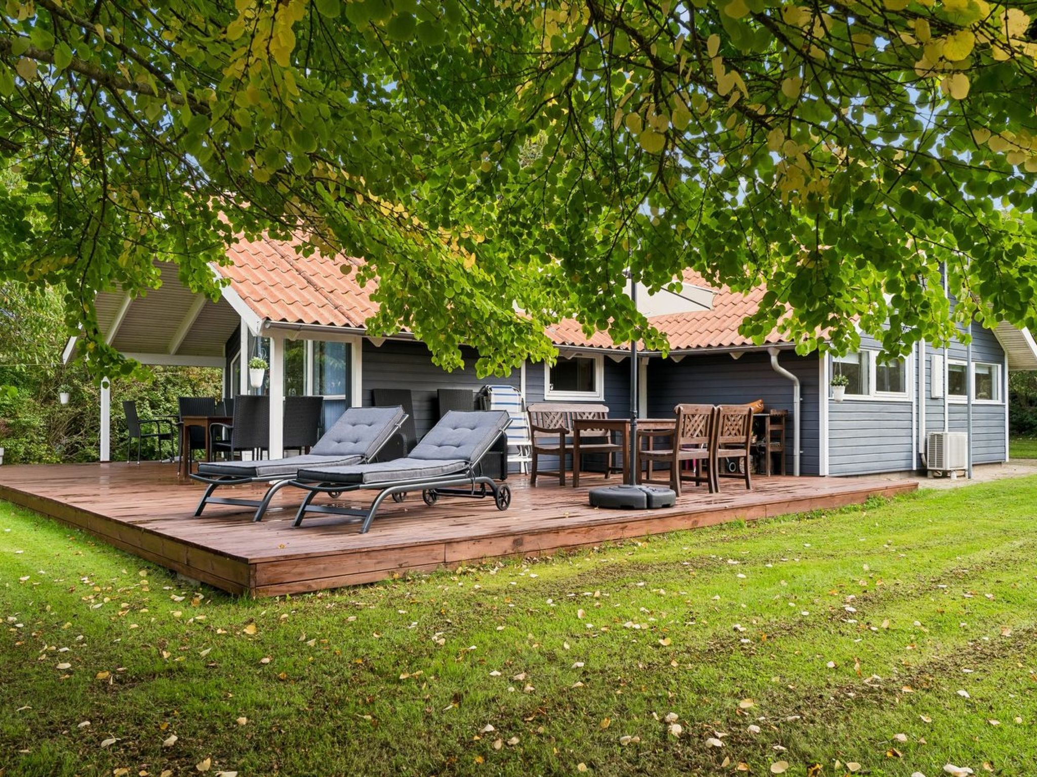 Ein Haus mit überdachter Terrasse, Gartenmöbeln und Rasenfläche.