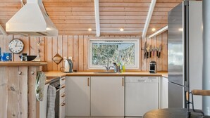 Une cuisine moderne avec des murs en bois, une fenêtre offrant une belle vue, un réfrigérateur en acier inoxydable et une bouilloire posée sur le plan de travail.