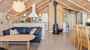 Un intérieur de chalet chaleureux avec un canapé, une table à manger, un plancher en bois, un coin cuisine et un poêle à bois.