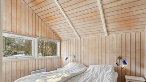 Une chambre avec des murs en bois, un lit, une fenêtre et deux lampes fixées au mur.