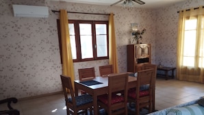 Een eetgedeelte met een houten tafel en stoelen, een bank, een kast en een raam met gordijnen.