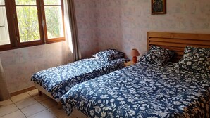 Een kamer met twee bedden, een raam met gordijnen, een hanglamp en een lijst met een foto aan de muur.