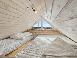 Un dormitorio acogedor y pequeño en el ático, con techo inclinado, una cama individual, una ventana con vista a barcos y una lámpara.