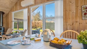 A wooden interior with a dining table set for breakfast, a kettle, and a basket of bread.