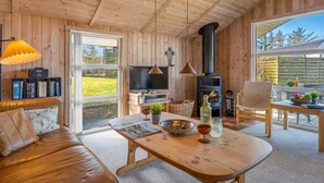 A cozy cabin interior with a sofa, wooden dining table, TV, and a fireplace.