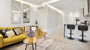 A modern living room with a yellow sofa, a coffee table, and a kitchen area with bar stools. - Golden Mile Lux Sea View Suite & Balcony (Marbella)