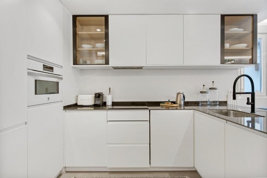 Eine moderne Küche mit weißen Schränken, einem eingebauten Ofen, einer Edelstahl-Spüle und einem Fenster über der Arbeitsplatte.
