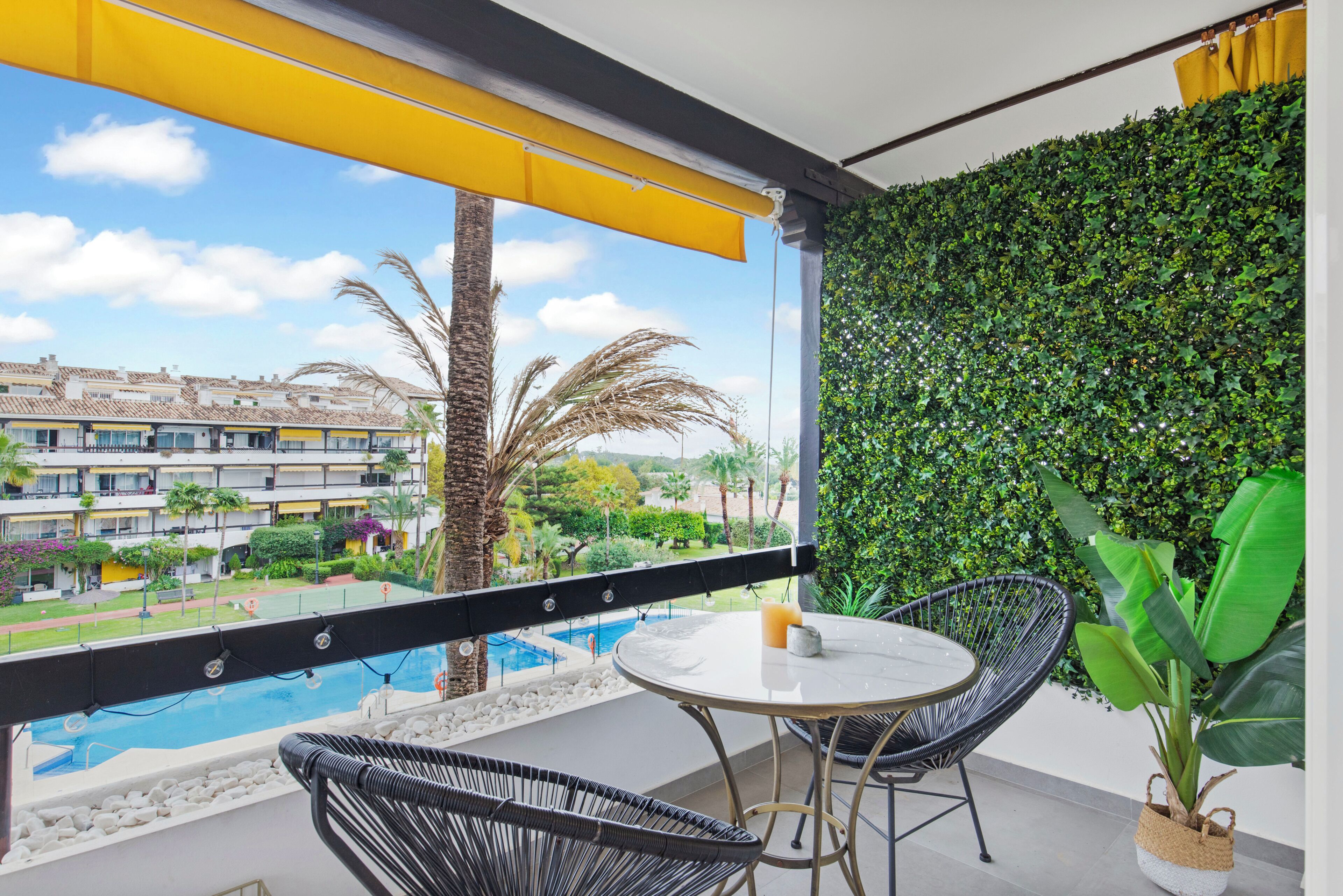 Ein Balkon mit Blick auf einen Swimmingpool, einem Tisch mit Stühlen und einer grünen Wand.