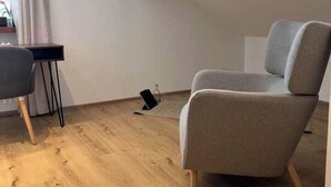 Une pièce avec un fauteuil à revêtement gris, une petite table et un plancher en bois.