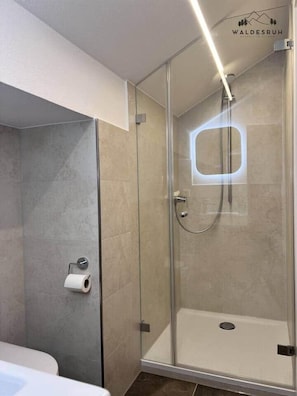 Een moderne badkamer met een douchecabine van glas, een toilet en een handdoekhouder.