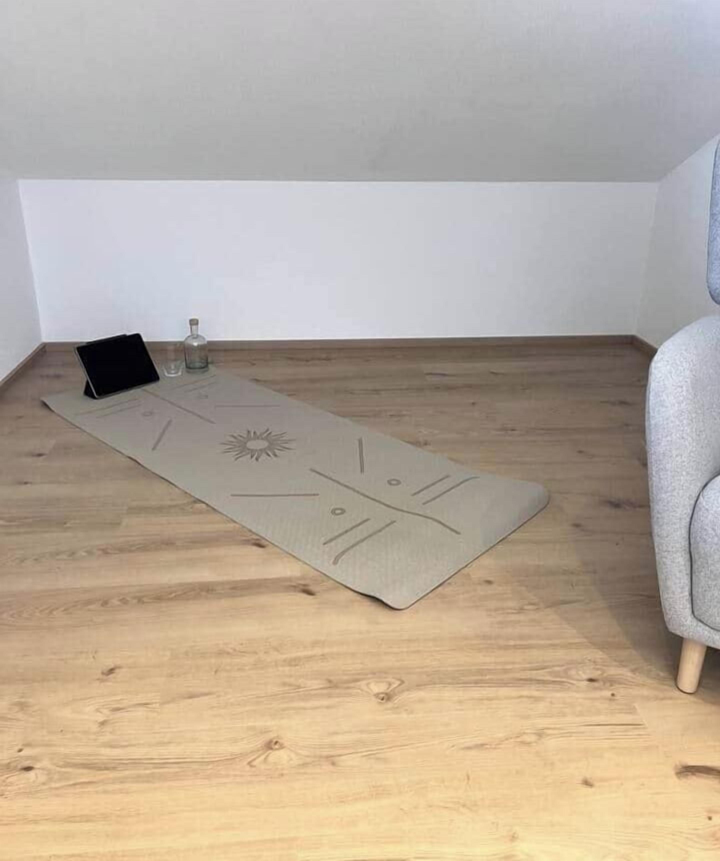 Et værelse med trægulv, en grå sofa og en tatamimåtte med en sort genstand og en glasflaske.