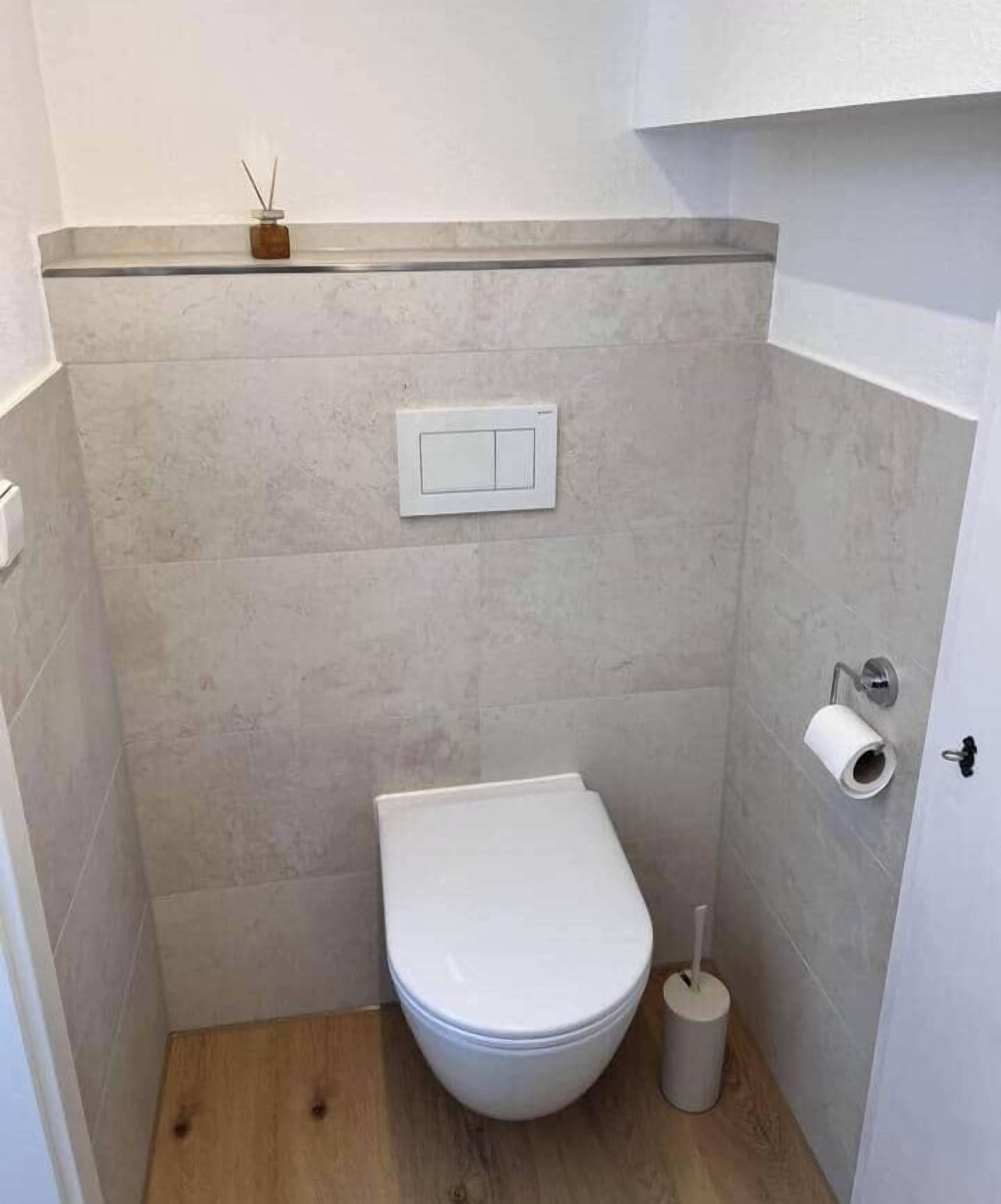 A small, modern bathroom with a toilet, a wall-mounted flush handle, and a toilet paper holder.