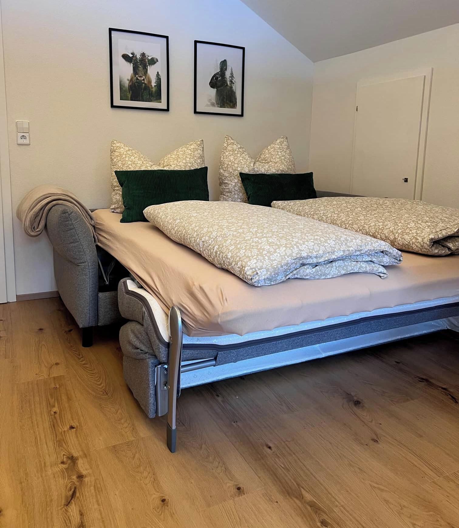 Ein Bett mit Matratze, Kissen und Kopfteil in einem Zimmer mit Holzboden und zwei gerahmten Bildern an der Wand.