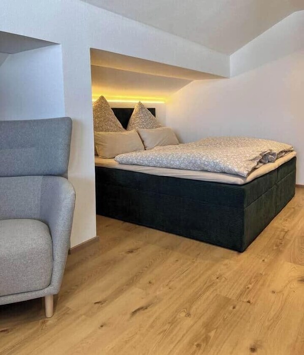 Et lille soveværelse med seng, stol og skråt loft.