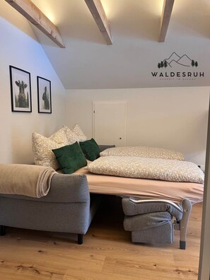 Een moderne slaapkamer met een bed, een bank en een rolstoel. Er hangen ingelijste foto's aan de muur en een logo op het plafond.
