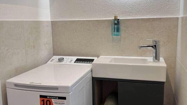 Une petite salle de bain équipée d’un lave-linge, d’un lavabo et d’un miroir.