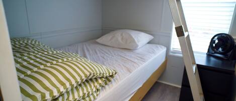 A bunk bed with a white mattress and green striped pillows, a wooden headboard, and a desk with a chair.