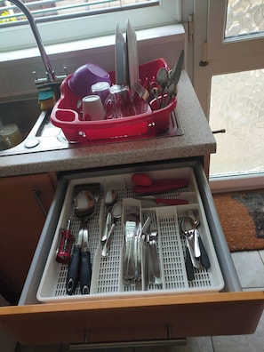 A kitchen with a dish rack holding various utensils and a drawer with neatly organized kitchen tools.