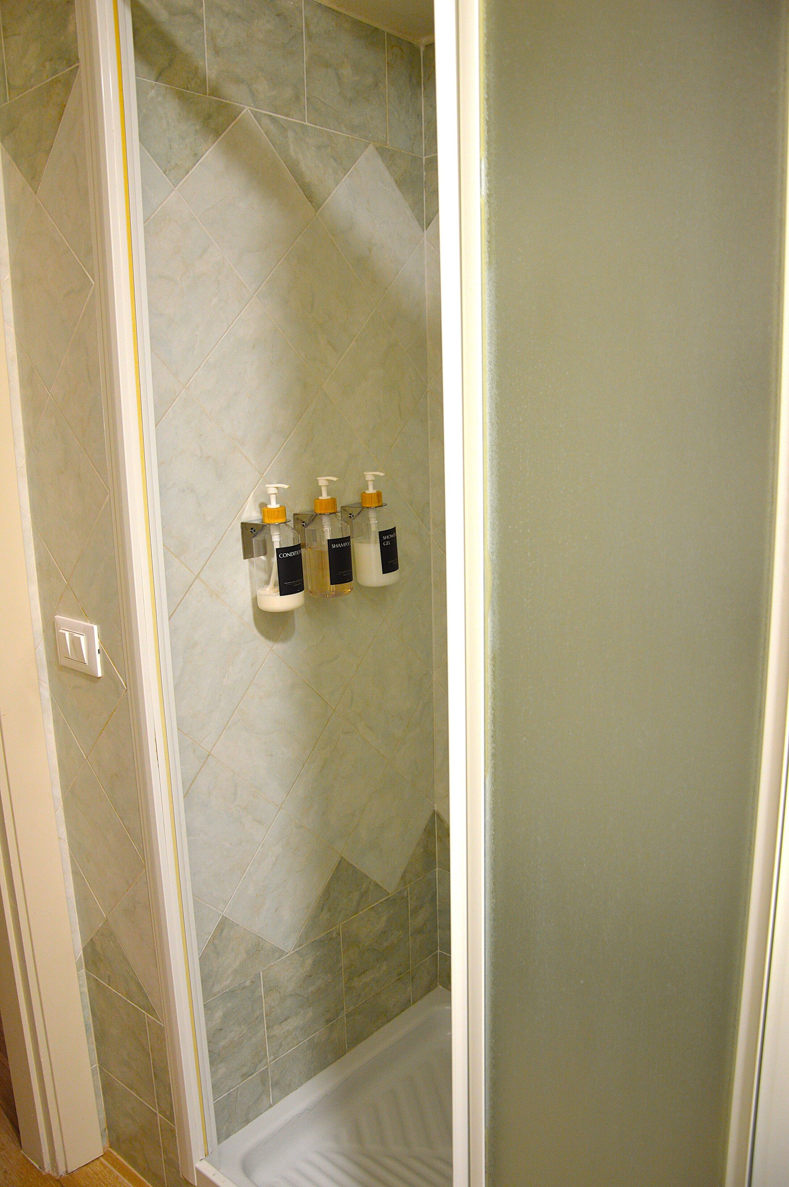 A bathroom with a shower area, tiled walls, and three bottles of liquid soap mounted on the wall.