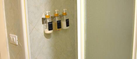 A bathroom with a shower area, tiled walls, and three bottles of liquid soap mounted on the wall.