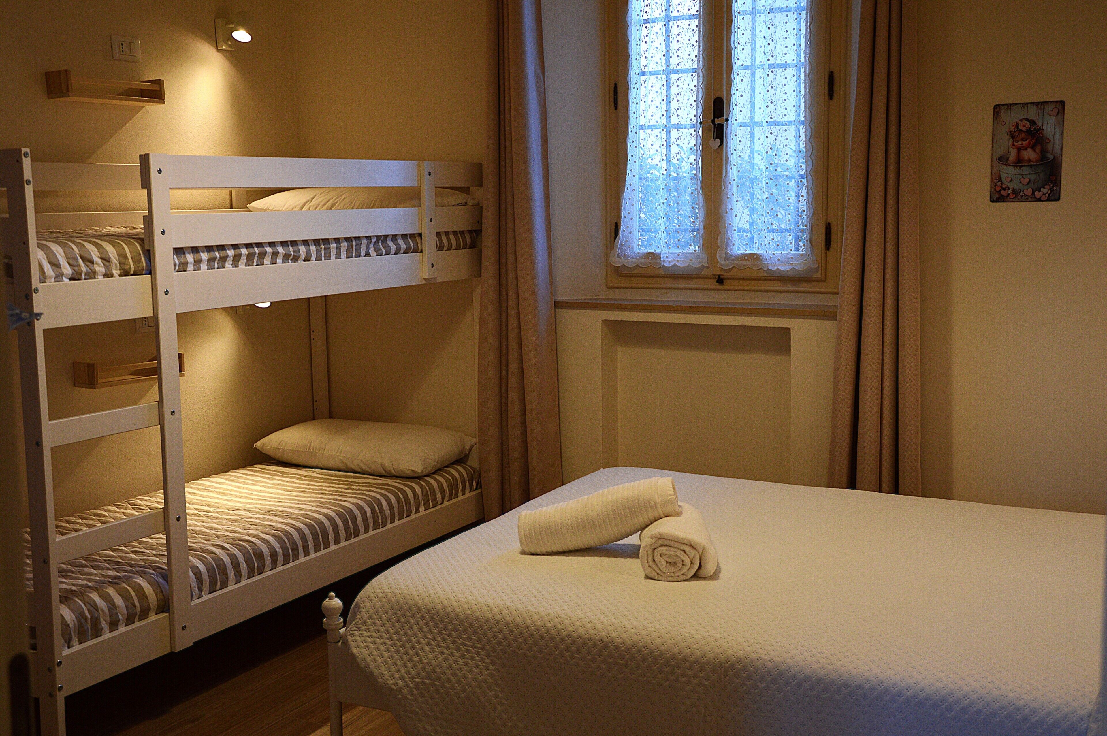 A bunk bed room with a single bed, a window with lace curtains, and a small picture on the wall.